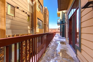 A narrow outdoor corridor with a metal railing, wooden siding buildings, and a clear sky.
