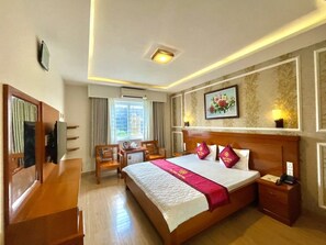 Una habitación de hotel con una cama grande, muebles de madera, un escritorio y una ventana con cortinas.