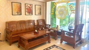 Una sala de estar con un sofá de madera, sillones y una mesa de centro. En la pared hay cuadros enmarcados con motivos florales.