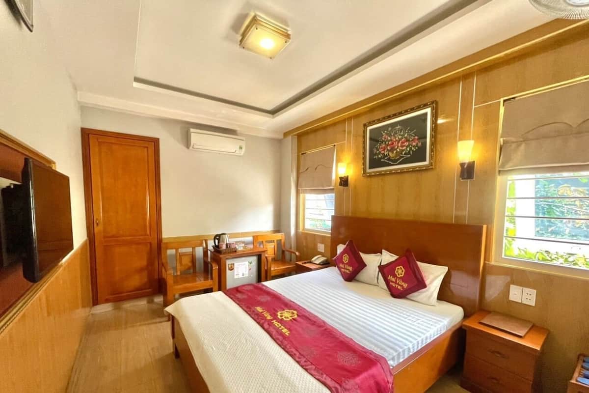 A hotel room with a large bed, wooden headboard, bedside tables, a desk with a chair, and a window with a view.