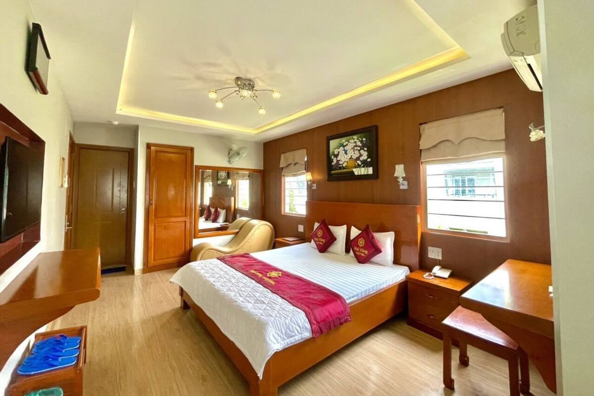 A hotel room with a large bed, a desk, a chair, a TV, and a window with a view of buildings.