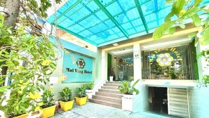 El exterior del Hotel Mai Vang, con techo azul, plantas en macetas y una escalera que lleva a la entrada.
