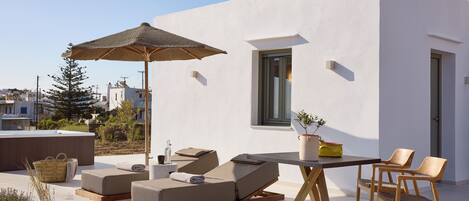 A modern outdoor lounge area with a table, chairs, and a large umbrella.