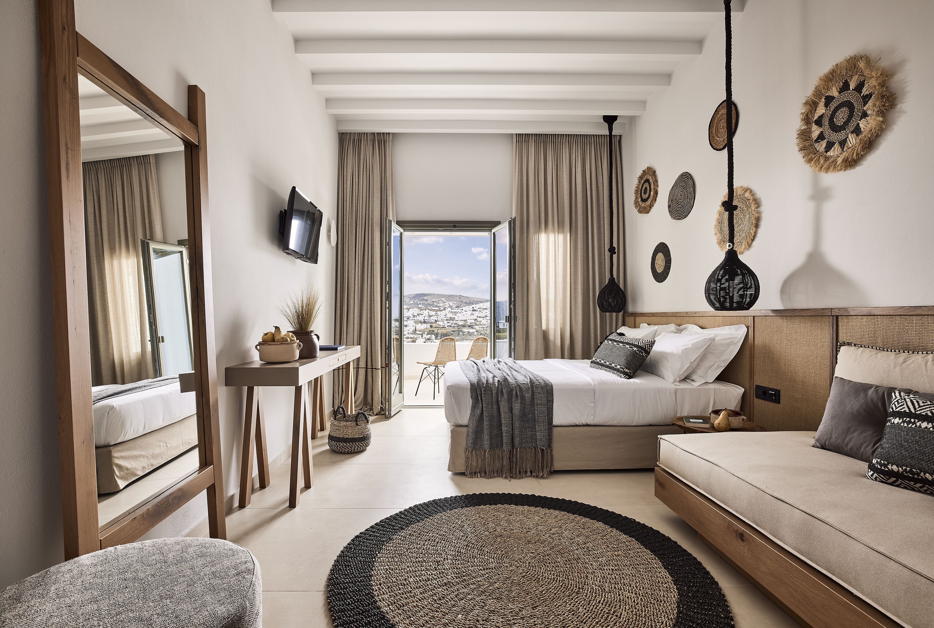 A modern bedroom with a large bed, a sofa, a desk, and a view of the city.
