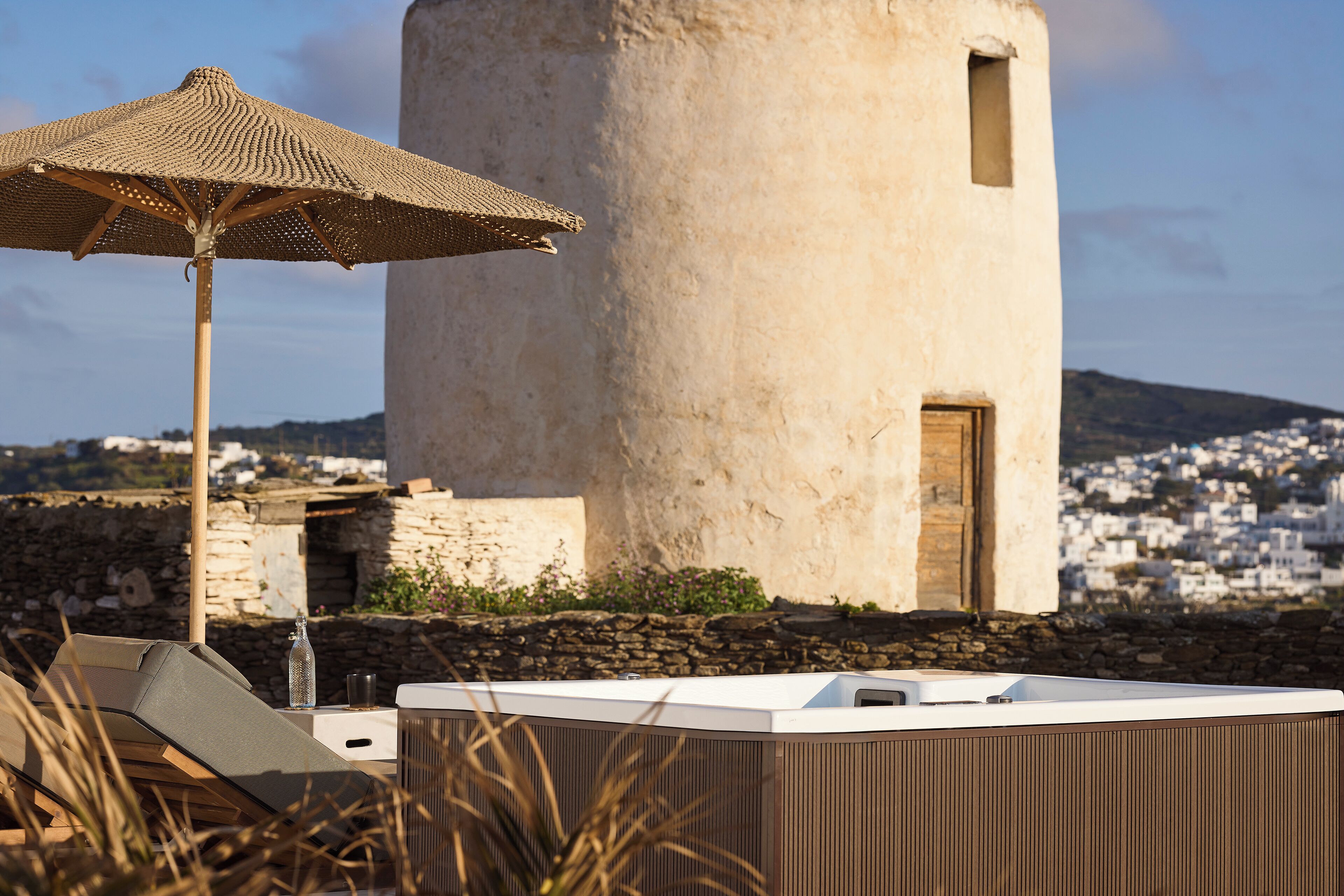 A stone tower with a door, a woven umbrella, and a modern outdoor seating area with a glass bottle.