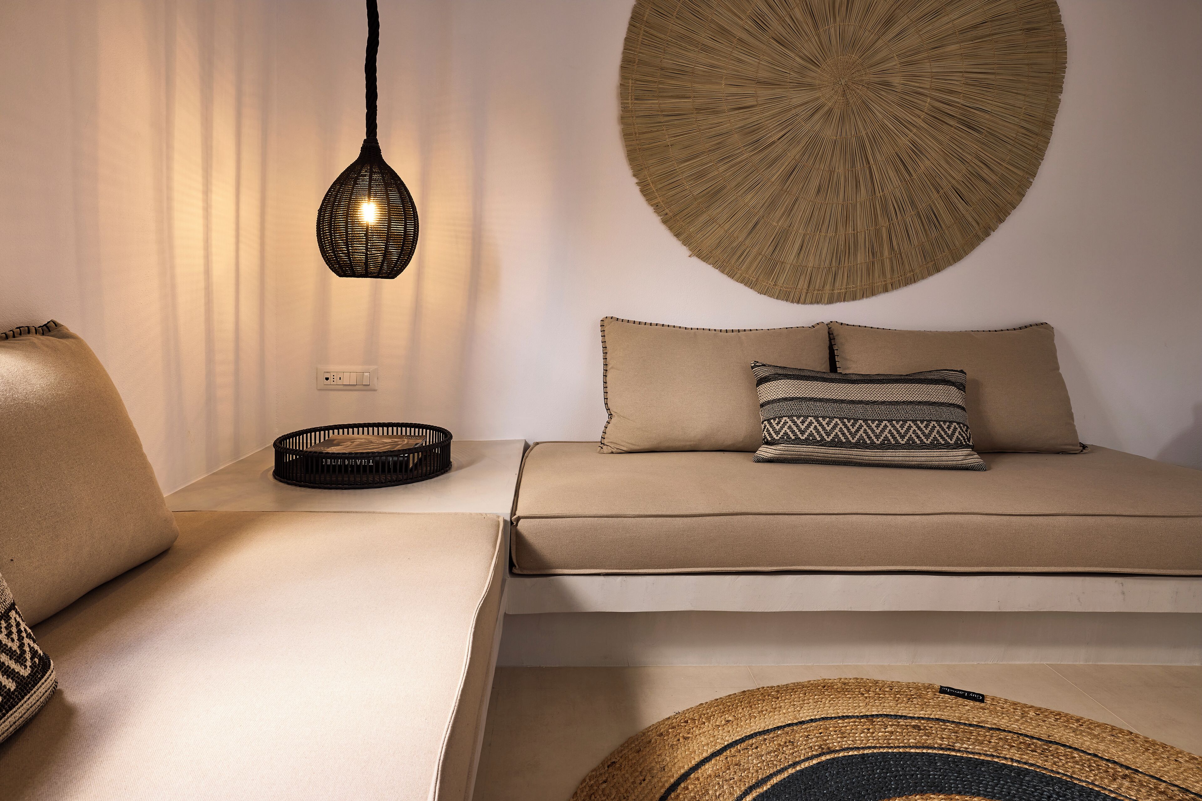A modern living room with a sofa, a hanging light fixture, and a woven wall art piece.