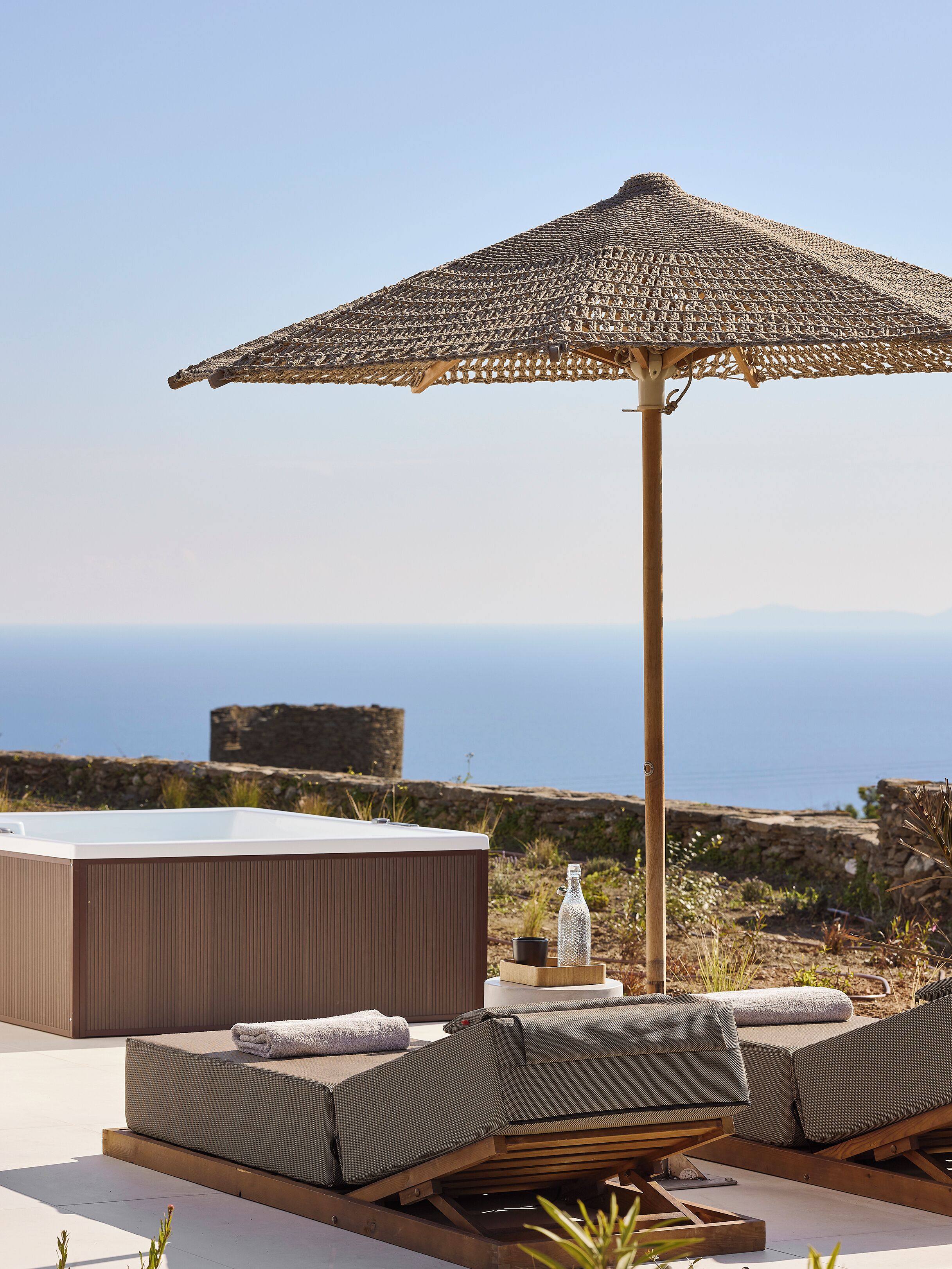 A rooftop terrace with a thatched umbrella, a hot tub, and a view of the sea.