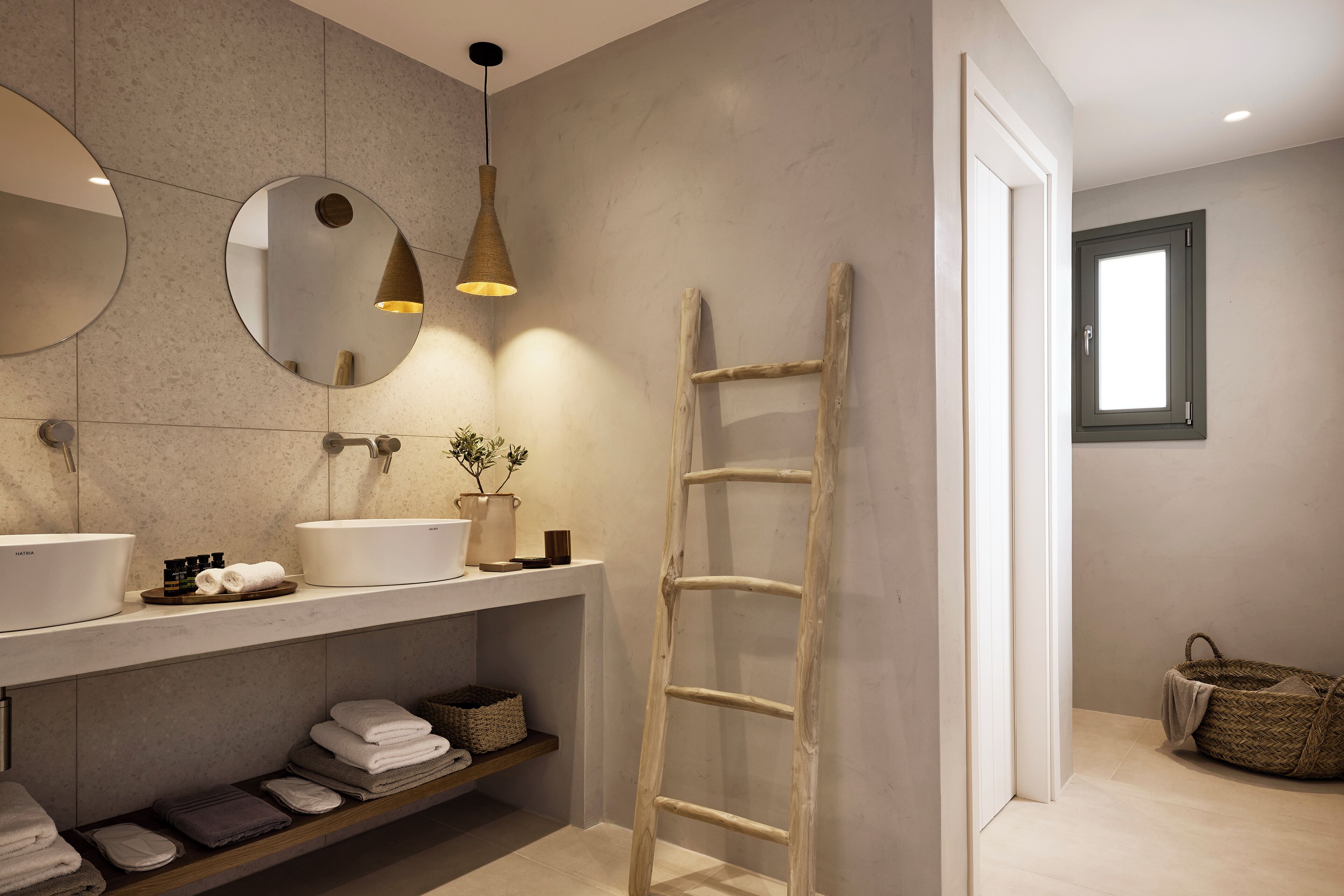 A modern bathroom with a large mirror, two sinks, a wooden ladder, and a window.