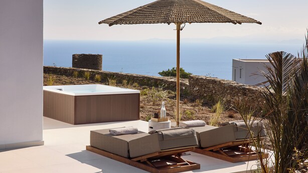 Terraza en la azotea con jacuzzi, sillas de descanso y sombrilla de paja.