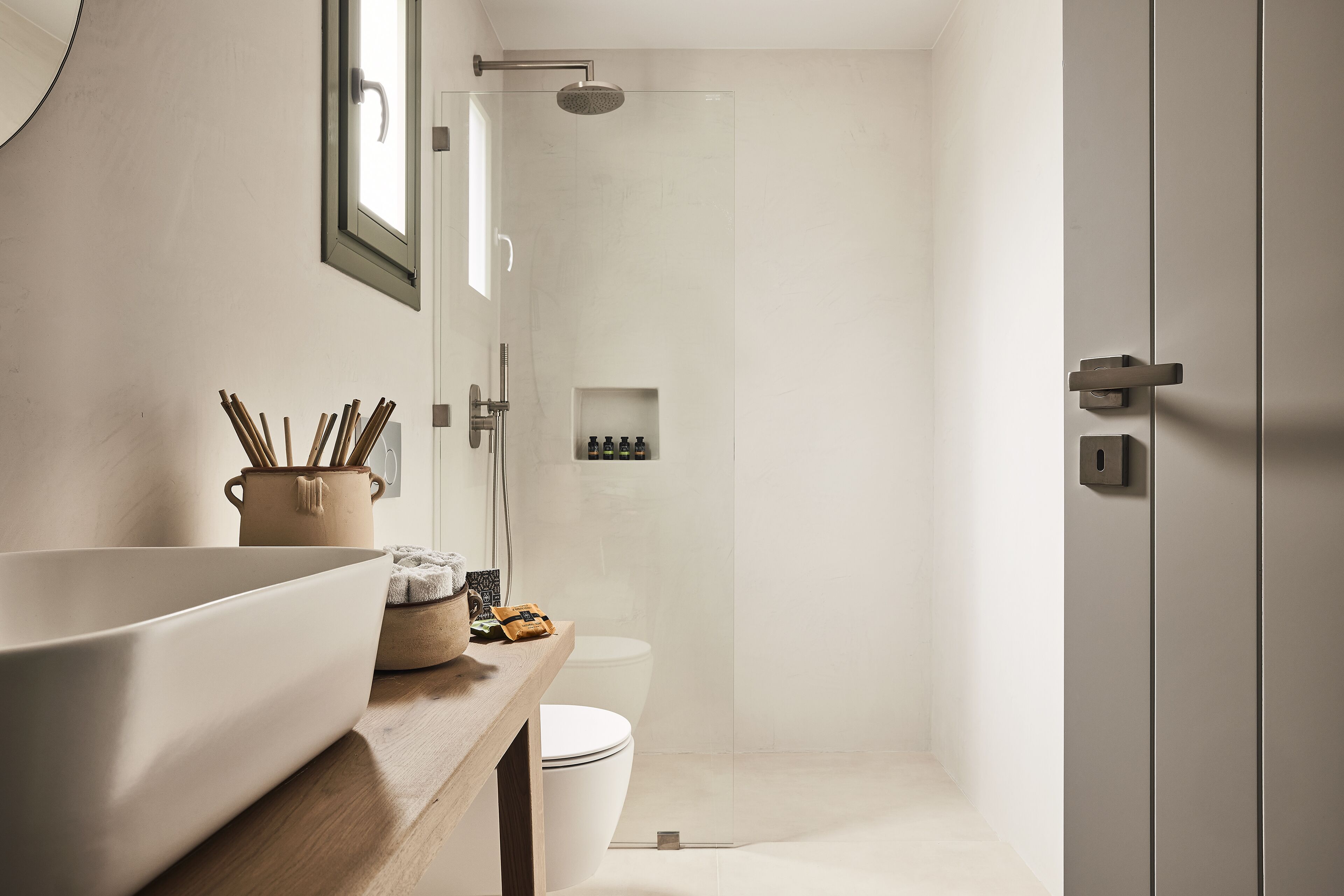 Une salle de bain moderne dotée d’un grand lavabo sur pied, d’un plan de toilette en bois, de toilettes et d’une douche à l’italienne.