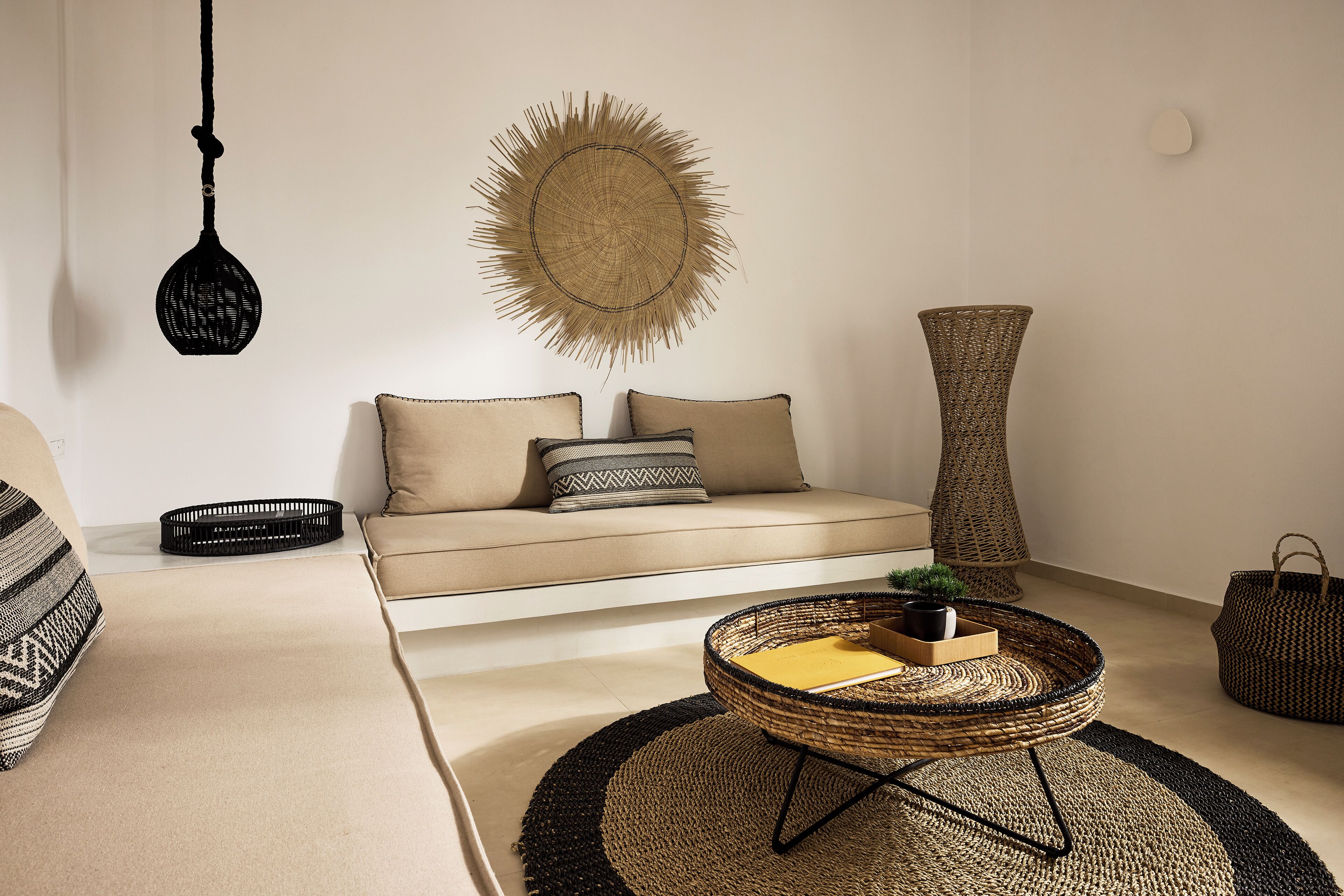 A living room with a sofa, a round woven coffee table, a tall woven vase, and a hanging light fixture.