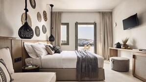Un dormitorio moderno con cama, mesitas de noche, televisor y vista a la ciudad.