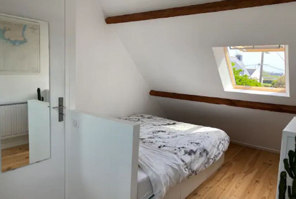 Una habitación pequeña con cama individual, techo inclinado, ventana con vistas y radiador.