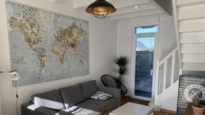 Ett modernt vardagsrum med en stor världskarta, en grå soffa, ett litet bord och en trappa som leder upp till ett övre plan.