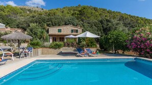 A swimming pool with lounge chairs and umbrellas, surrounded by greenery and a hillside. - Cal Cristo, Villa with private pool in a quiet area (Pollensa)