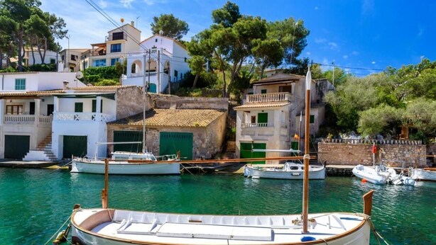 A coastal scene with a row of white buildings with green shutters, a clear blue sky, and several boats docked in the water. - Cal Cristo, Villa with private pool in a quiet area (Pollensa)