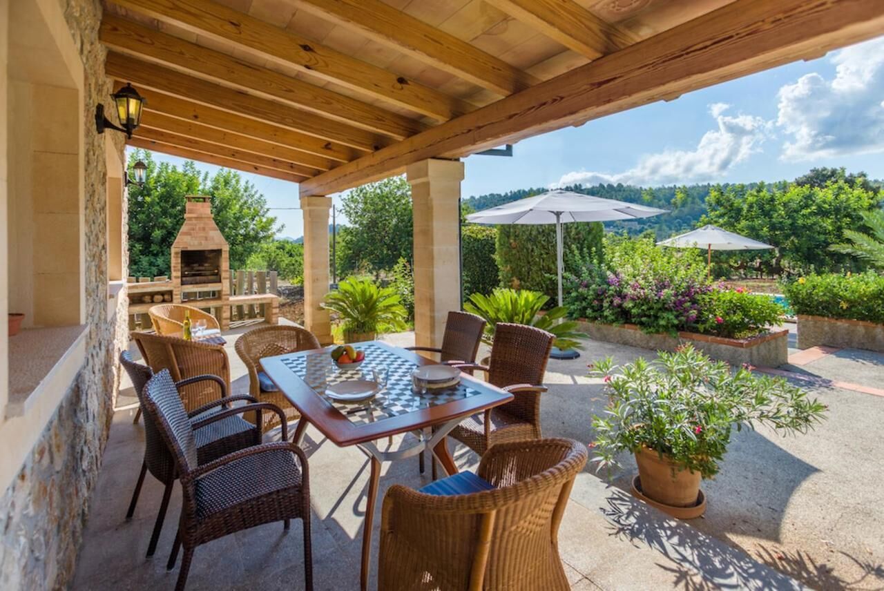 Une terrasse extérieure agrémentée d’une pergola en bois, d’un four en briques, de meubles en osier et de plantes en pot.