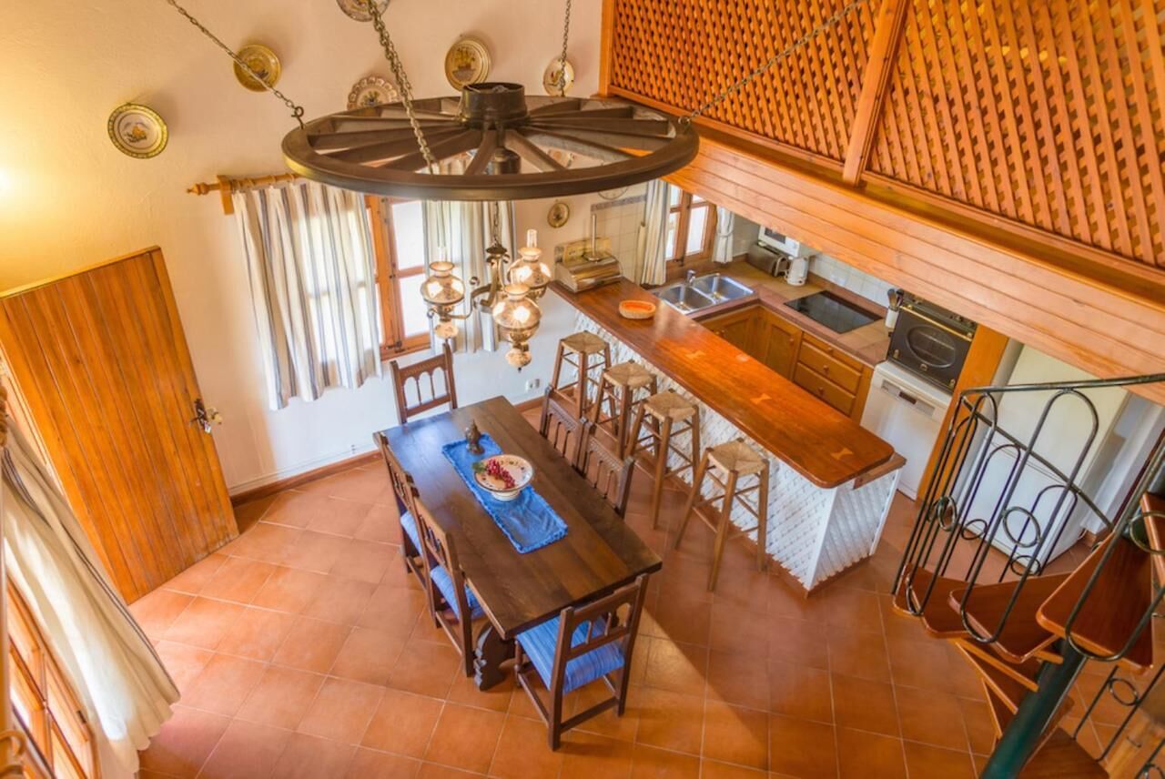Een eethoek met een houten tafel en stoelen, een keuken met een spoelbak en fornuis, en een spiltrap.