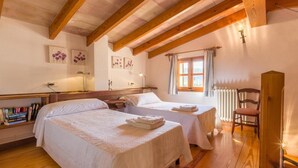 A bedroom with two beds, wooden beams, a window with curtains, and a radiator. - Cal Cristo, Villa with private pool in a quiet area (Pollensa)