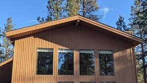 A modern wooden cabin with large windows and a deck area with outdoor furniture. - Home nestled in the forest just outside Sisters (Deschutes County)