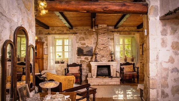 Una habitación rústica con paredes de piedra, vigas de madera, una chimenea y un espejo grande.
