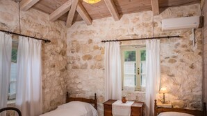 Una habitación rústica con paredes de piedra, dos camas de madera, un aparador de madera y una ventana con cortinas.