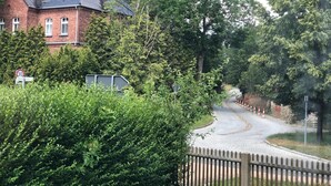 A brick building with a curved driveway, surrounded by dense greenery and a wooden fence. - beautiful place in the village (Elsteraue)