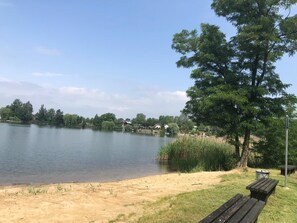 Ein Park am Seeufer mit Sandstrand, einer Holzbank und einem Picknicktisch.