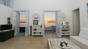 Ein Wohnzimmer mit Fernseher, einem Couchtisch mit Pralinen und Blick auf den Sonnenuntergang durch geöffnete Türen.