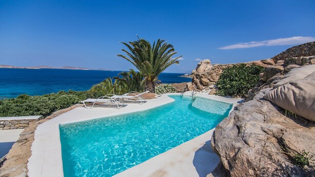 Ein Pool mit klarem, blauem Wasser, umgeben von Felsen und Palmen, mit Blick auf das Meer.