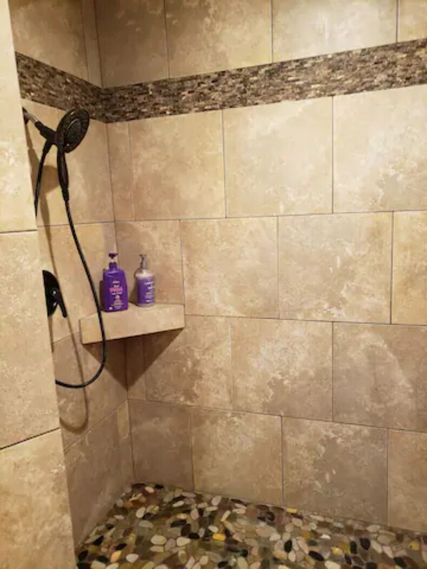 A shower area with beige tiles, a showerhead, and a shelf with two bottles.