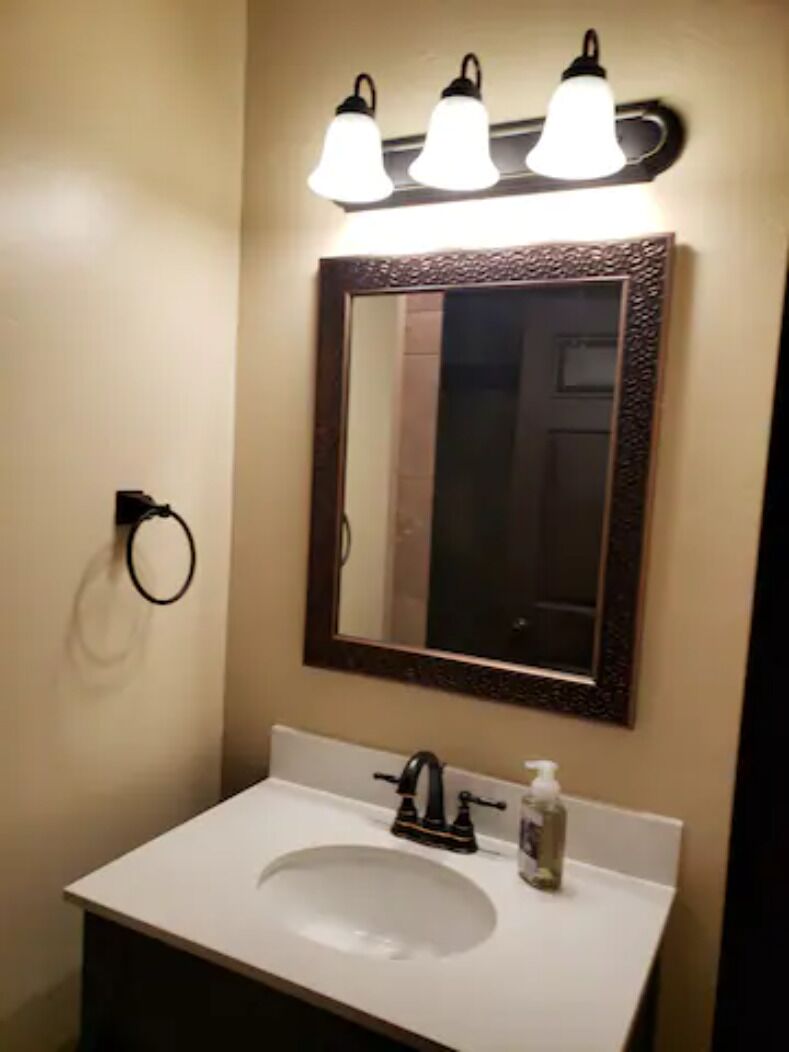 A bathroom with a white sink, a mirror with a dark frame, and three wall-mounted lights.