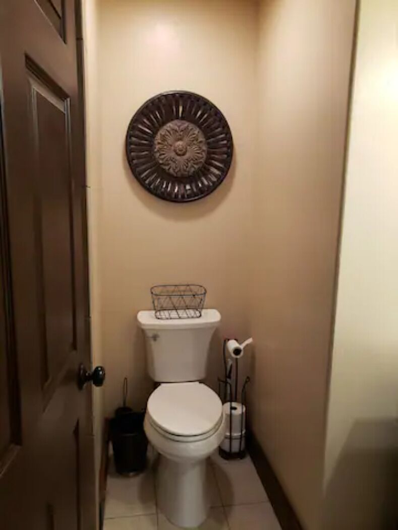 A narrow bathroom with a toilet, a decorative wall piece above it, and a trash can beside the toilet.