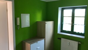 Ein Zimmer mit grünen Wänden, einem weißen Heizkörper, einem Fenster mit weißen Rahmen, einem weißen Schrank und einer weißen Tür.