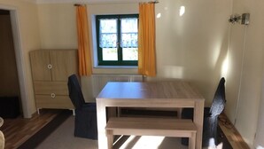 Ein Zimmer mit einem Holztisch und zwei Stühlen, einem Fenster mit Vorhängen und einer Heizung.
