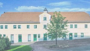 Ein zweistöckiges Gebäude mit flachem Dach, grünen Türen und Fenstern.