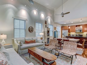 A modern living room with a sofa, coffee table, and chairs, a dining area with a table and chairs, and a kitchen with appliances.