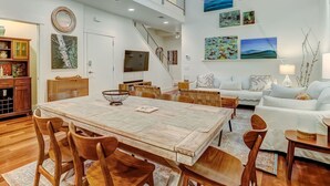Amplia sala de estar con una mesa de comedor, sillas de madera, un sofá y una escalera que conduce a un nivel superior.