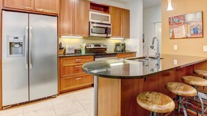Una cocina moderna con armarios de madera, electrodomésticos de acero inoxidable, una isla integrada con taburetes y un cuadro en la pared.