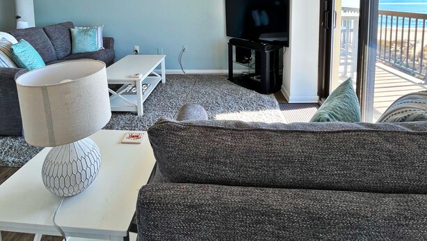 A living room with a sofa, a coffee table, a lamp, a TV, and a view of the ocean. - Ocean & Bay Views, Resort Amenities, Weekly Activities & Fireworks! - Book Now (Ocean City)