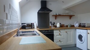 A modern kitchen with a built-in oven, microwave, and sink. There is a wooden countertop, a black range hood, and a washing machine. - Idyllic rural retreat - Generous ferry discounts available (Isle of Wight)