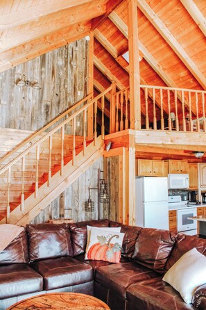 A rustic wooden interior with a staircase, a leather sofa, and a kitchen area.