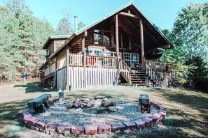 A wooden cabin with a porch, a fire pit, and a stone wall.