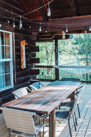 A wooden deck with a table and chairs, a hammock, and a hanging sign.