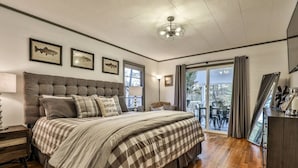 A bedroom with a large bed, a nightstand, a lamp, a chandelier, framed fish pictures on the wall, and a view of the outdoors through a sliding glass door.
