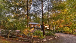A cabin surrounded by dense forest with a gravel driveway leading to the entrance.