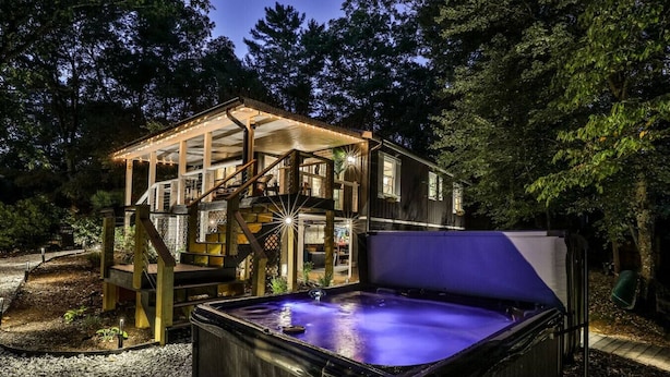A hot tub in a forested area with a wooden deck and stairs leading to a house.