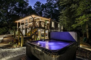 Un bain à remous situé dans un espace boisé, avec une terrasse en bois et des escaliers menant à une maison.
