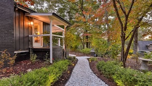 A pathway leading to a house with a porch, surrounded by trees and a garden.