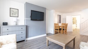 A modern living room with a grey wall, a flat-screen TV, a wooden dining table, and a grey sofa. - Platform Holderness House (Hull)